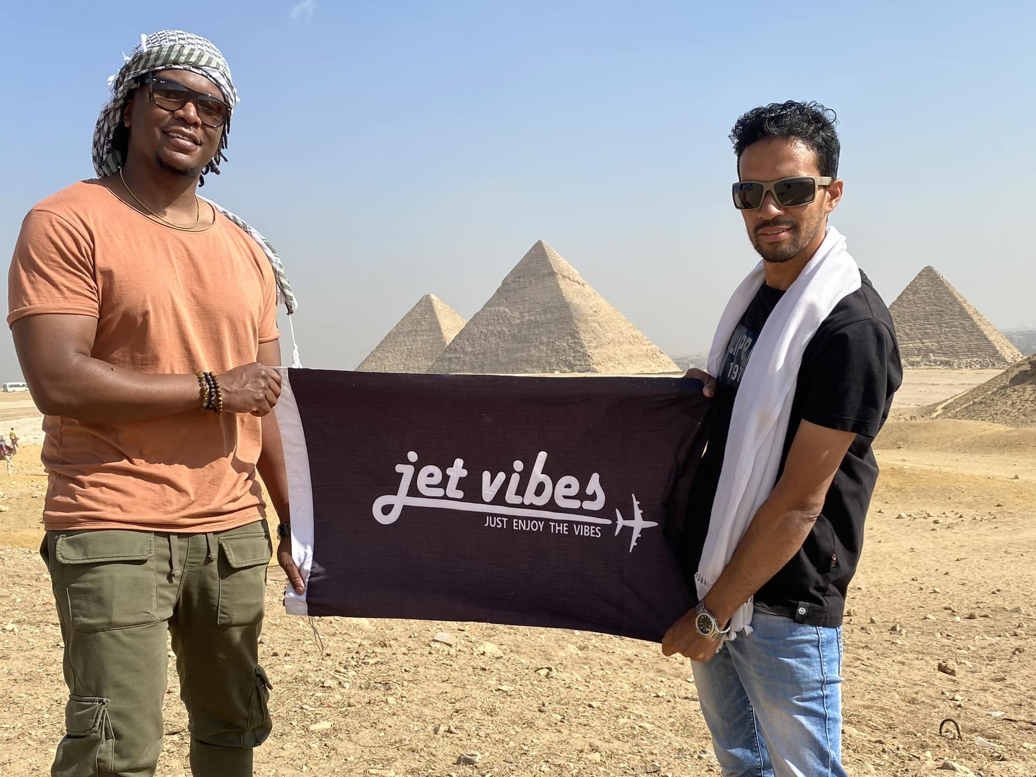 Jet Vibes founder with companion holding brand flag in front of the pyramids in Egypt
