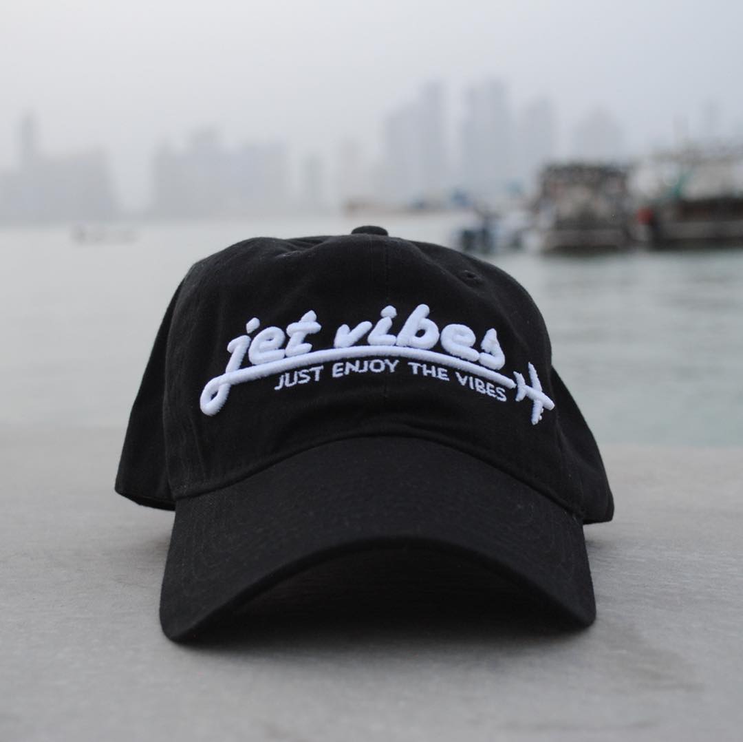 Jet Vibes black hat with embroidered white logo photographed outdoors