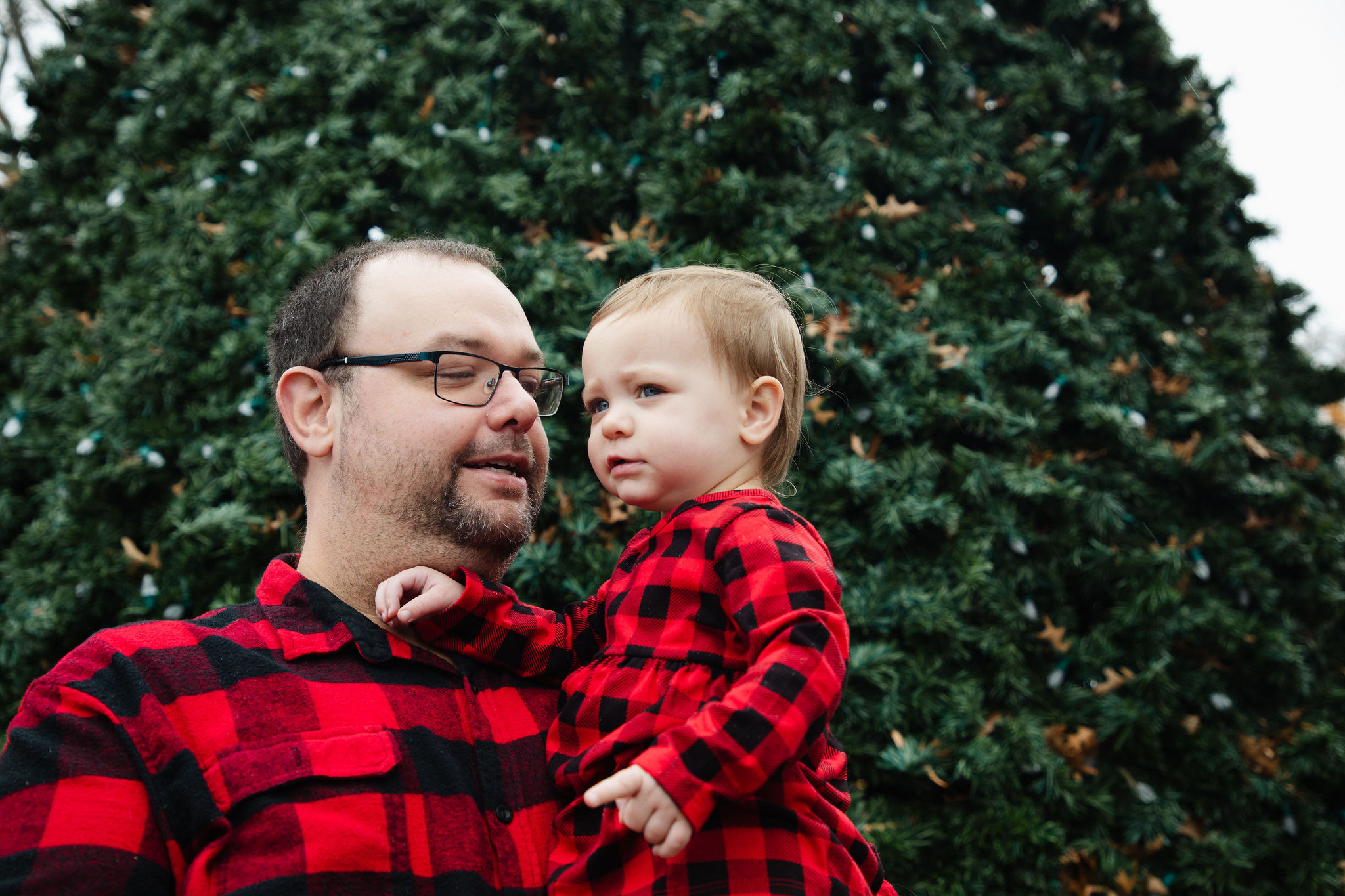 Father holding his toddler while she gazes thoughtfully at the surroundings — candid holiday portrait by Karmil Studios