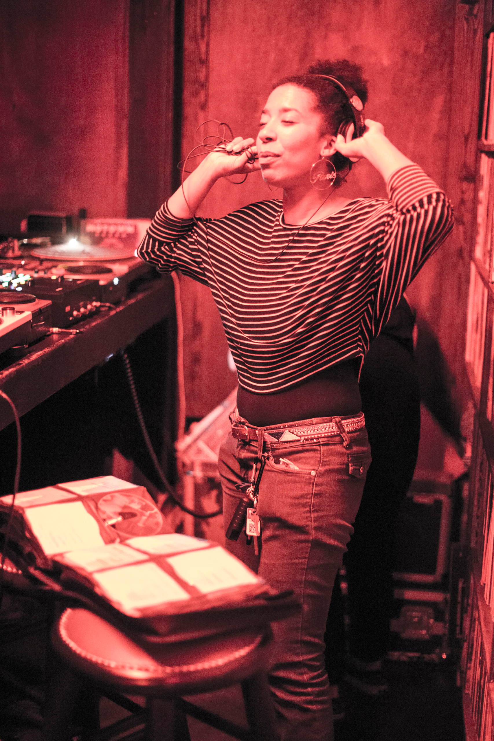 DJ adjusting headphones with eyes closed beside full DJ booth setup at D.A.M.E. event — Karmil Studios