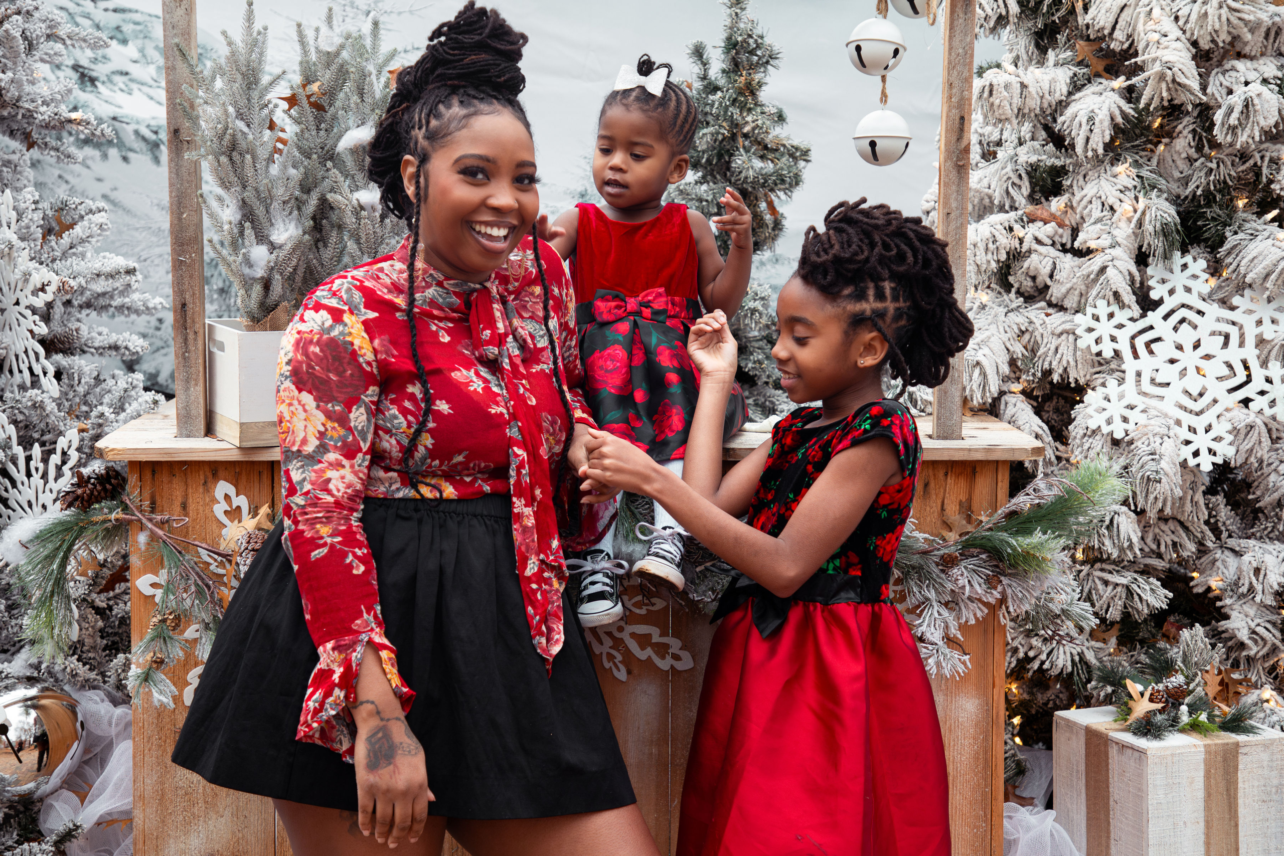 Mother and daughters sharing candid moment in front of snowy Christmas backdrop during holiday portrait session