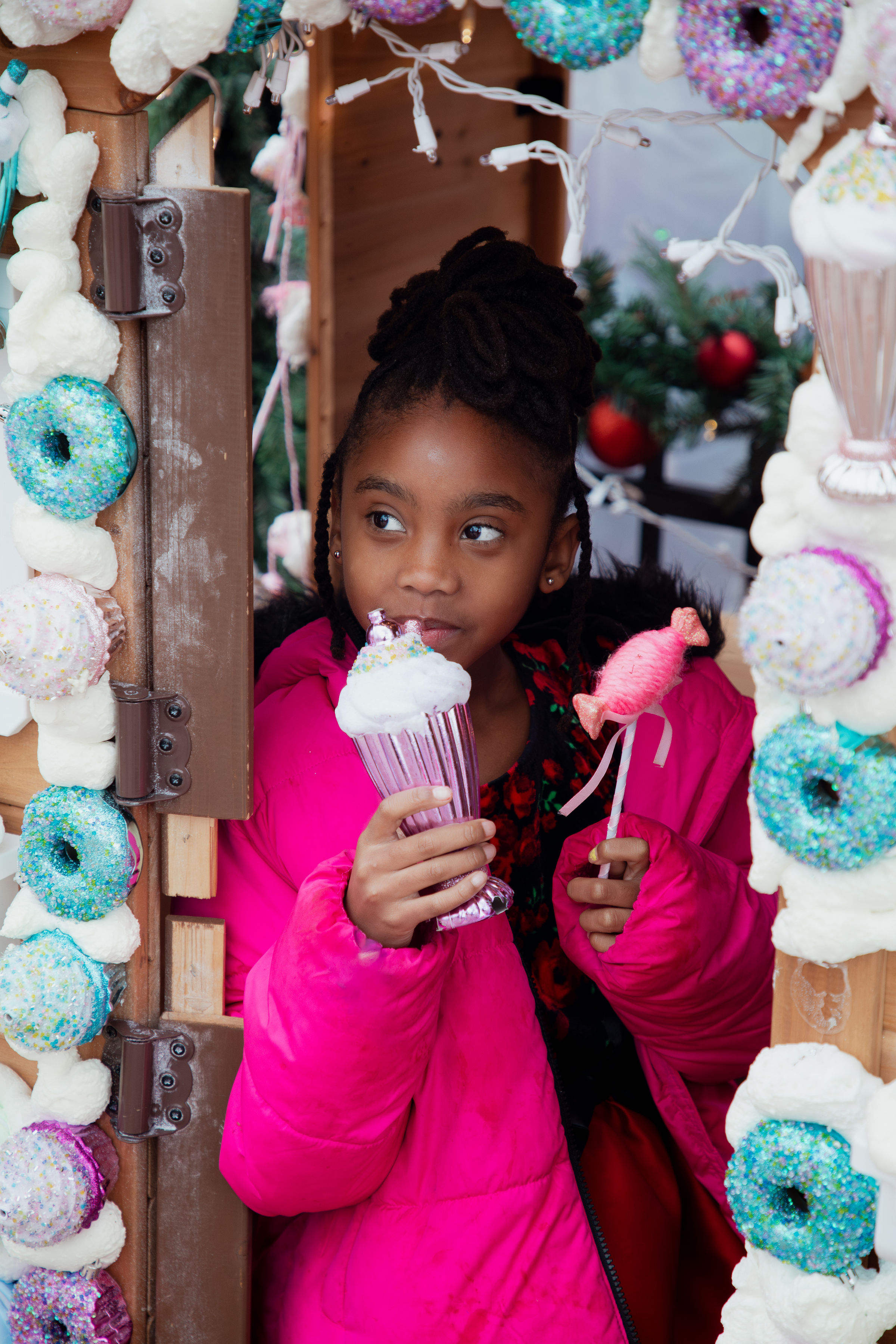 Young girl holding holiday treats inside festive Christmas candy house during portrait session