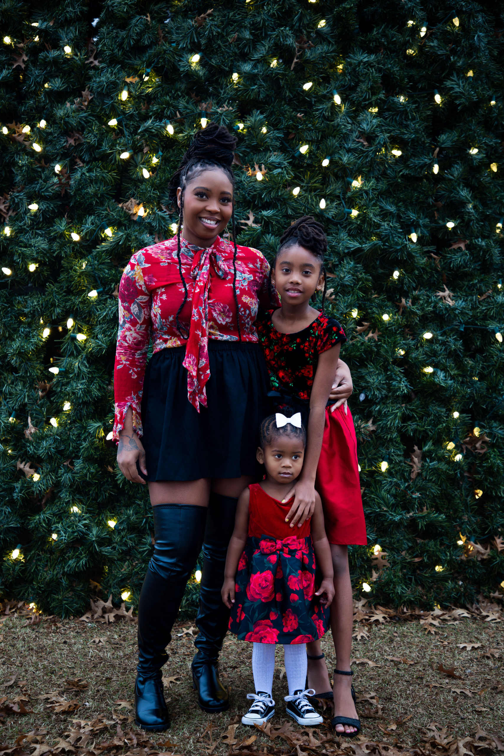 Mother and daughters posing together in front of glowing Christmas tree lights during holiday portrait session