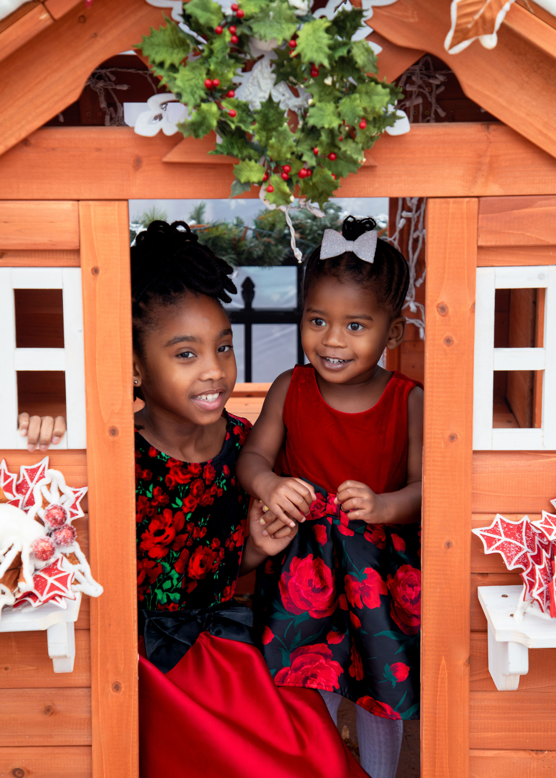 Sisters smiling together inside wooden Christmas playhouse during holiday family session