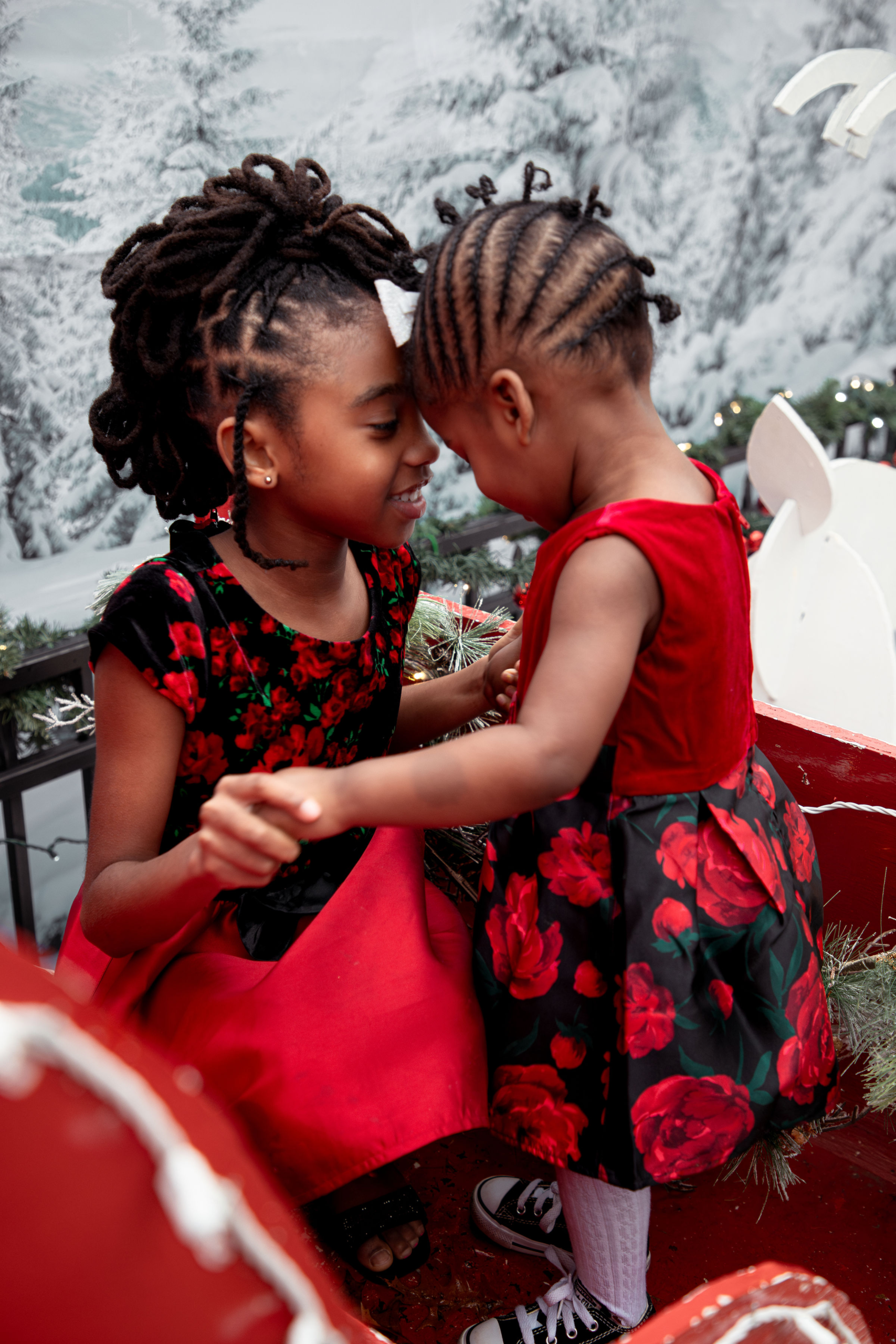 Sisters sharing a sweet moment together inside red Christmas sleigh during holiday photo session