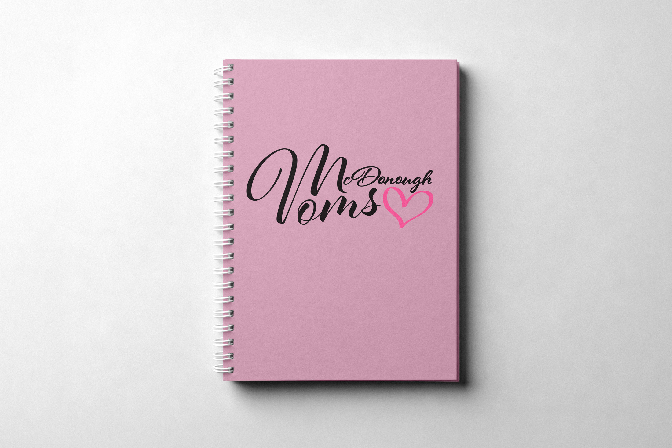 McDonough Moms logo applied to a pink spiral notebook mockup as part of the brand identity system.